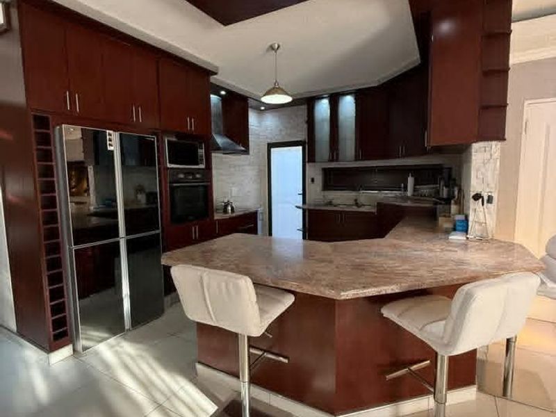 A modern kitchen featuring dark wood cabinetry, stone countertops, a breakfast bar, and integrated appliances with recessed lighting and tiled flooring.