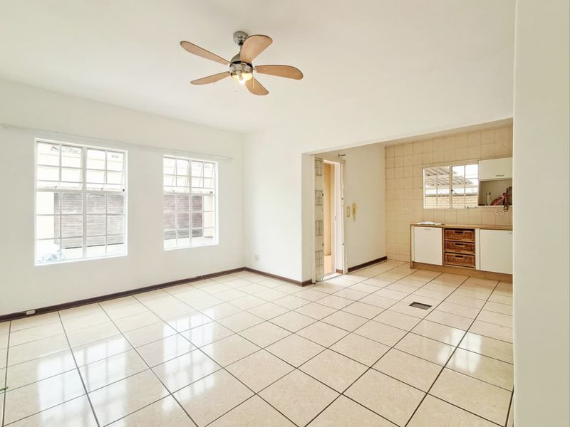Open-plan living area featuring tiled flooring, a ceiling fan, and a functional kitchen corner with built-in cabinetry and tiled backsplash.