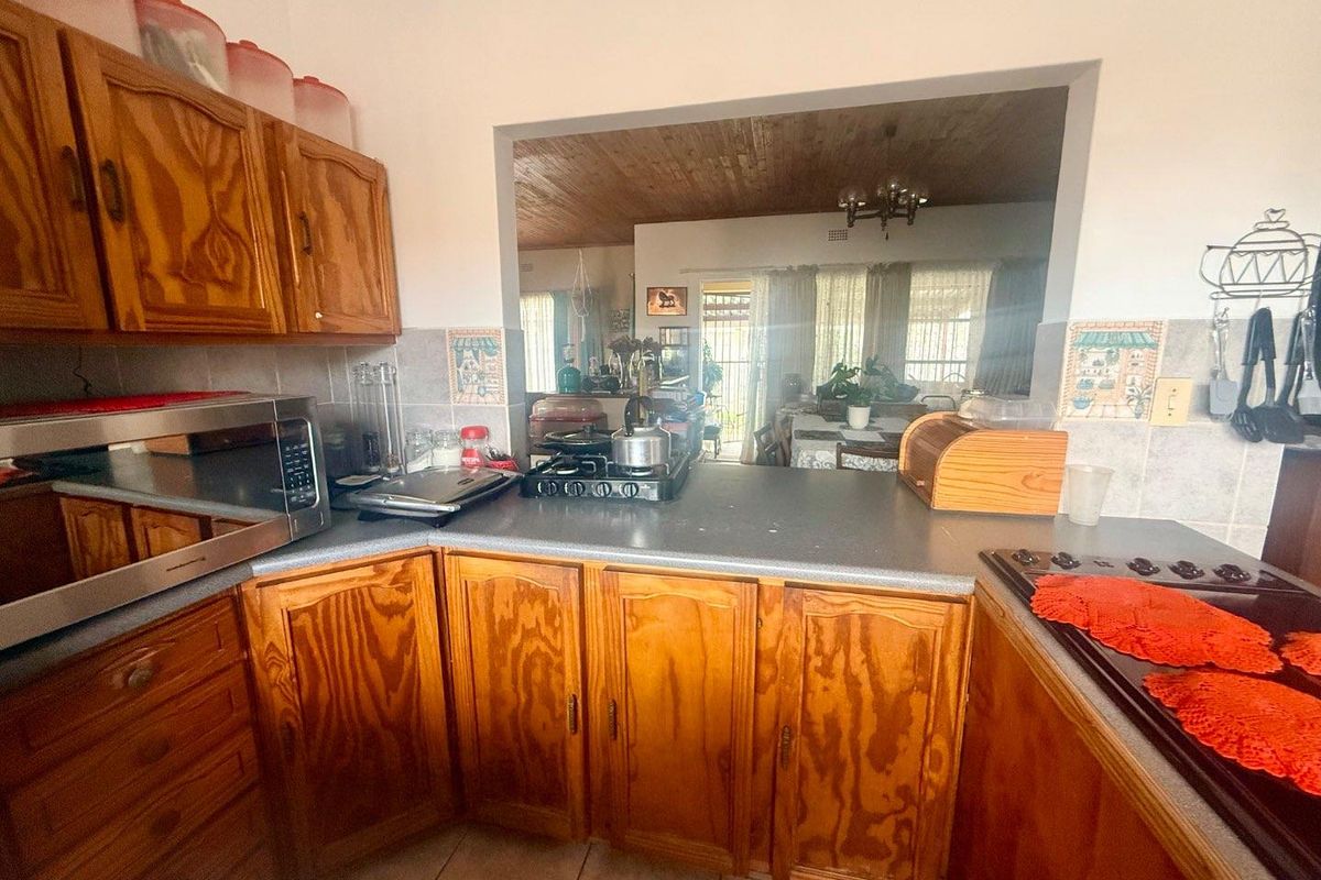 A functional kitchen featuring traditional timber cabinetry, laminate countertops, and a convenient serving hatch opening into the adjacent living area.