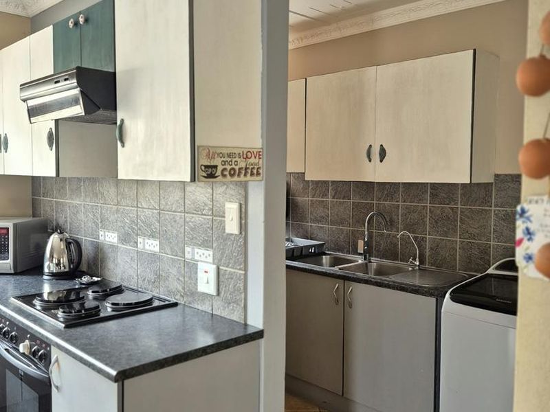 Functional kitchen featuring built-in cabinetry, electric hob, oven, extractor fan, and double bowl sink with tiled backsplash and flooring.