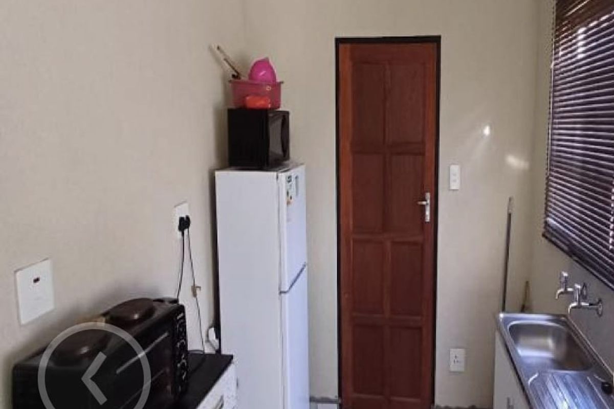 A functional kitchen area featuring a stainless steel sink, tiled flooring, and a wooden door leading to an adjacent space.