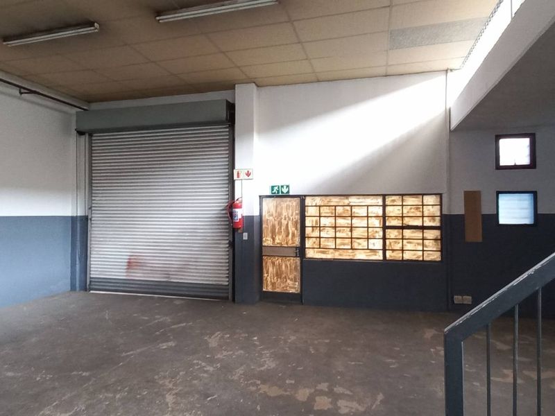 Spacious industrial utility area featuring a large roller shutter door, concrete flooring, and a metal staircase leading to an upper level.