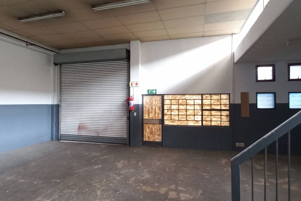 Spacious industrial utility area featuring a large roller shutter door, concrete flooring, and a metal staircase leading to an upper level.