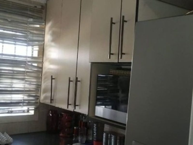 A functional kitchen area featuring built-in cabinetry, a window with security bars, and integrated microwave space, offering a practical layout for daily use.