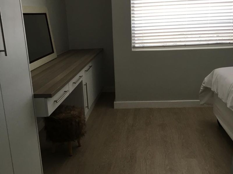 A well-maintained bedroom featuring modern laminate flooring, a built-in vanity unit, integrated wardrobe storage, and venetian blinds for light control.