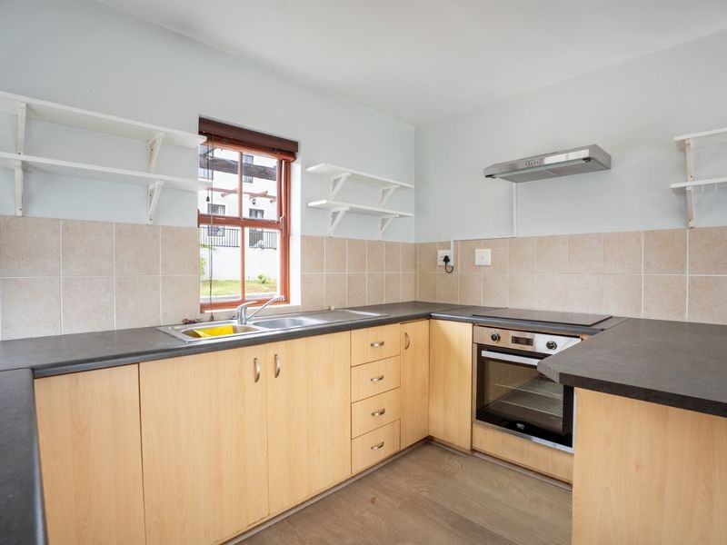 A functional kitchen featuring light wood cabinetry, dark laminate countertops, built-in oven with hob, extractor fan, and tiled backsplash.