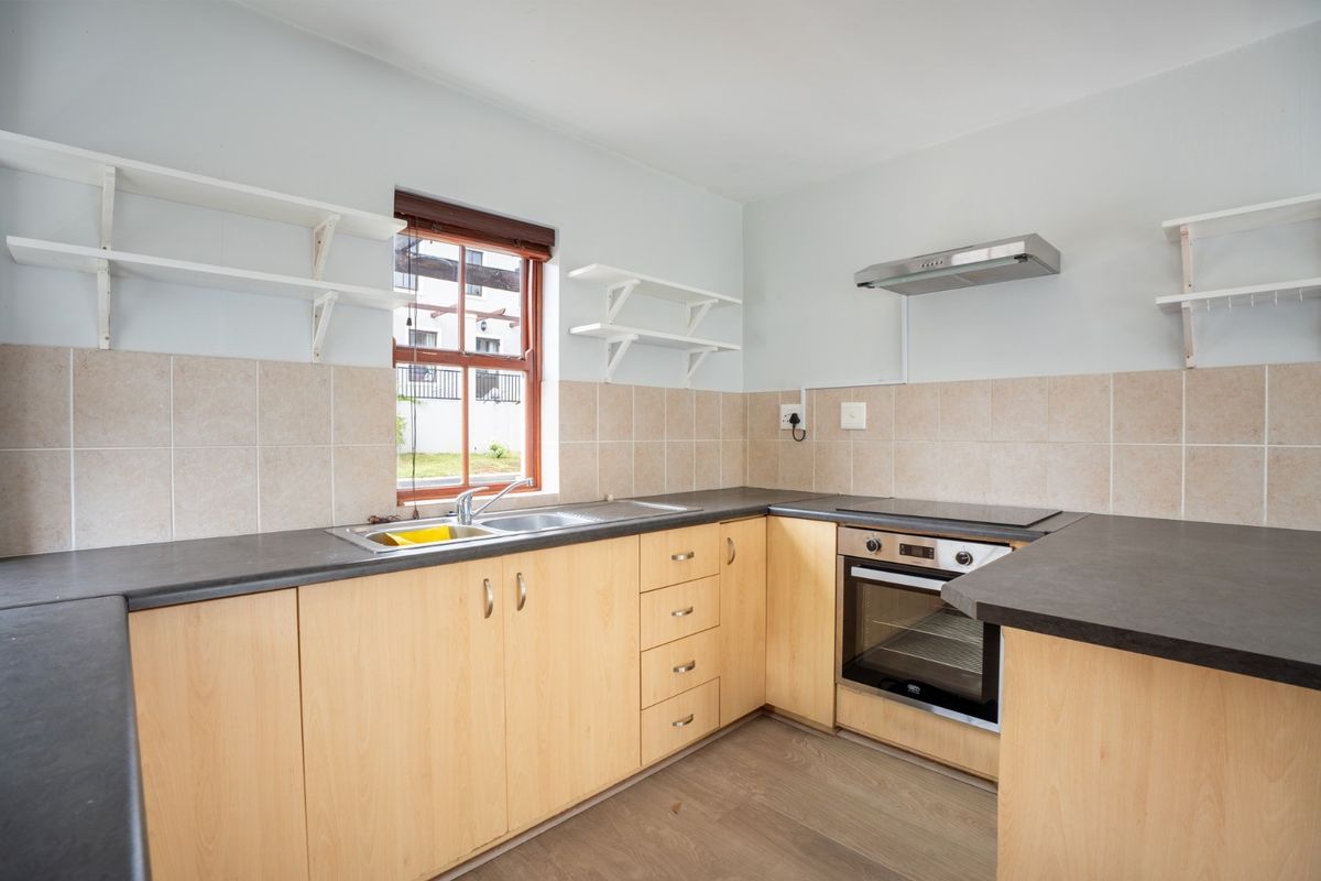A functional kitchen featuring light wood cabinetry, dark laminate countertops, built-in oven with hob, extractor fan, and tiled backsplash.