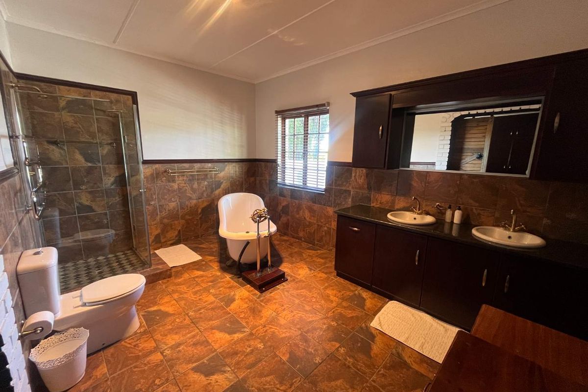Spacious bathroom featuring a double vanity with dark cabinetry, a glass-enclosed shower, a freestanding bathtub, and tiled flooring throughout.