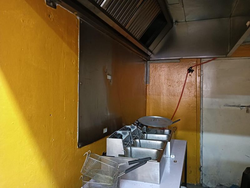 Commercial kitchen prep area featuring a stainless steel extractor hood, splashback, and deep fryer setup with yellow painted walls.