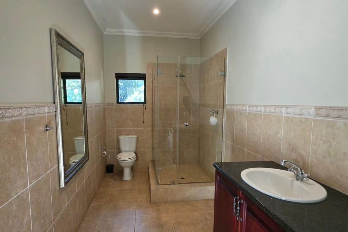 A well-maintained bathroom featuring a glass-enclosed shower, a vanity with a granite countertop, and neutral wall tiling.
