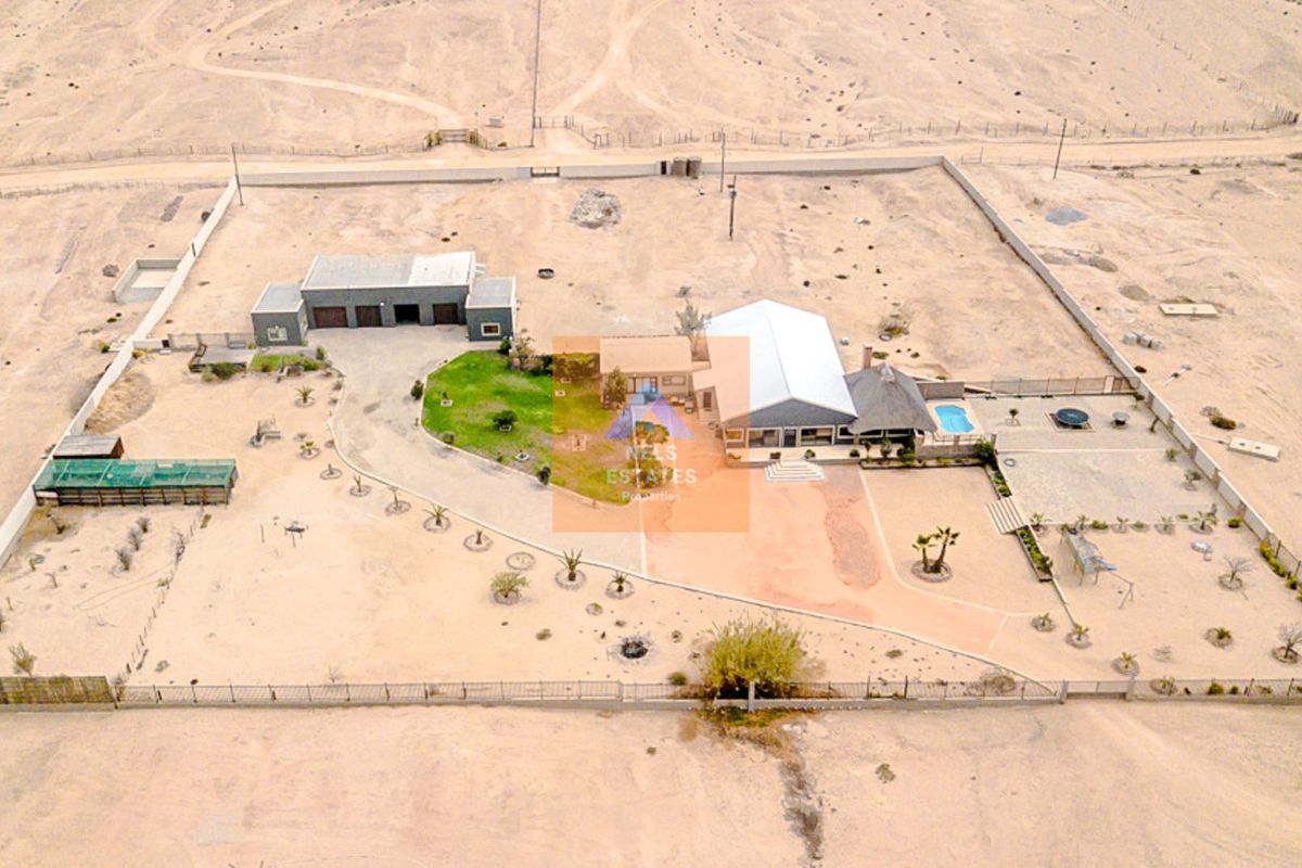 Aerial view of a large residential property featuring a main house, detached garage, swimming pool, and expansive fenced grounds in a desert landscape.