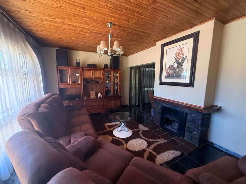 A cozy living room featuring a stone-clad fireplace, timber-clad ceiling, and tiled flooring, with sliding glass doors leading to an adjacent space.