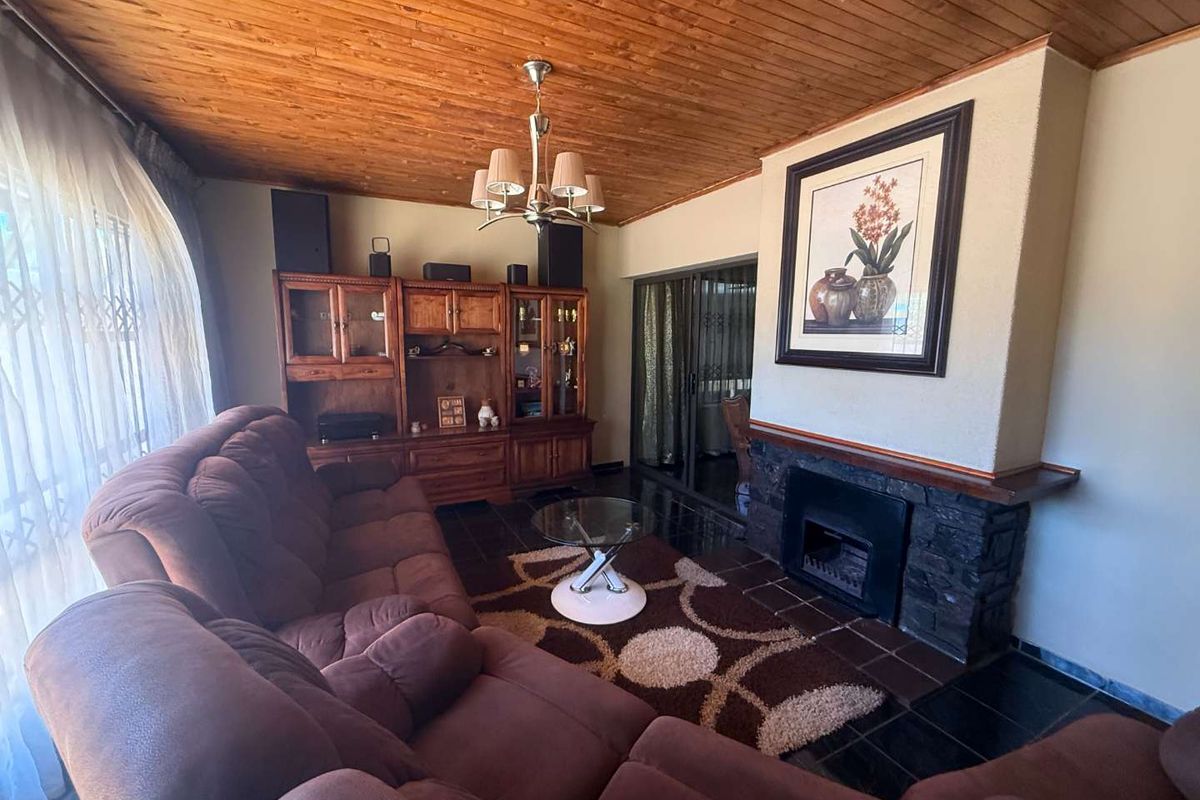A cozy living room featuring a stone-clad fireplace, timber-clad ceiling, and tiled flooring, with sliding glass doors leading to an adjacent space.