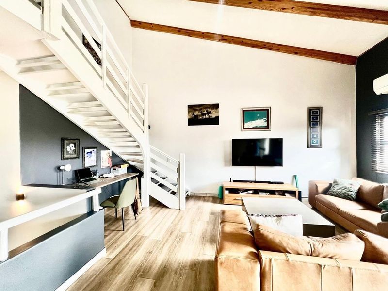 Spacious living room featuring high ceilings with exposed timber beams, a built-in staircase, and a dedicated workspace area.