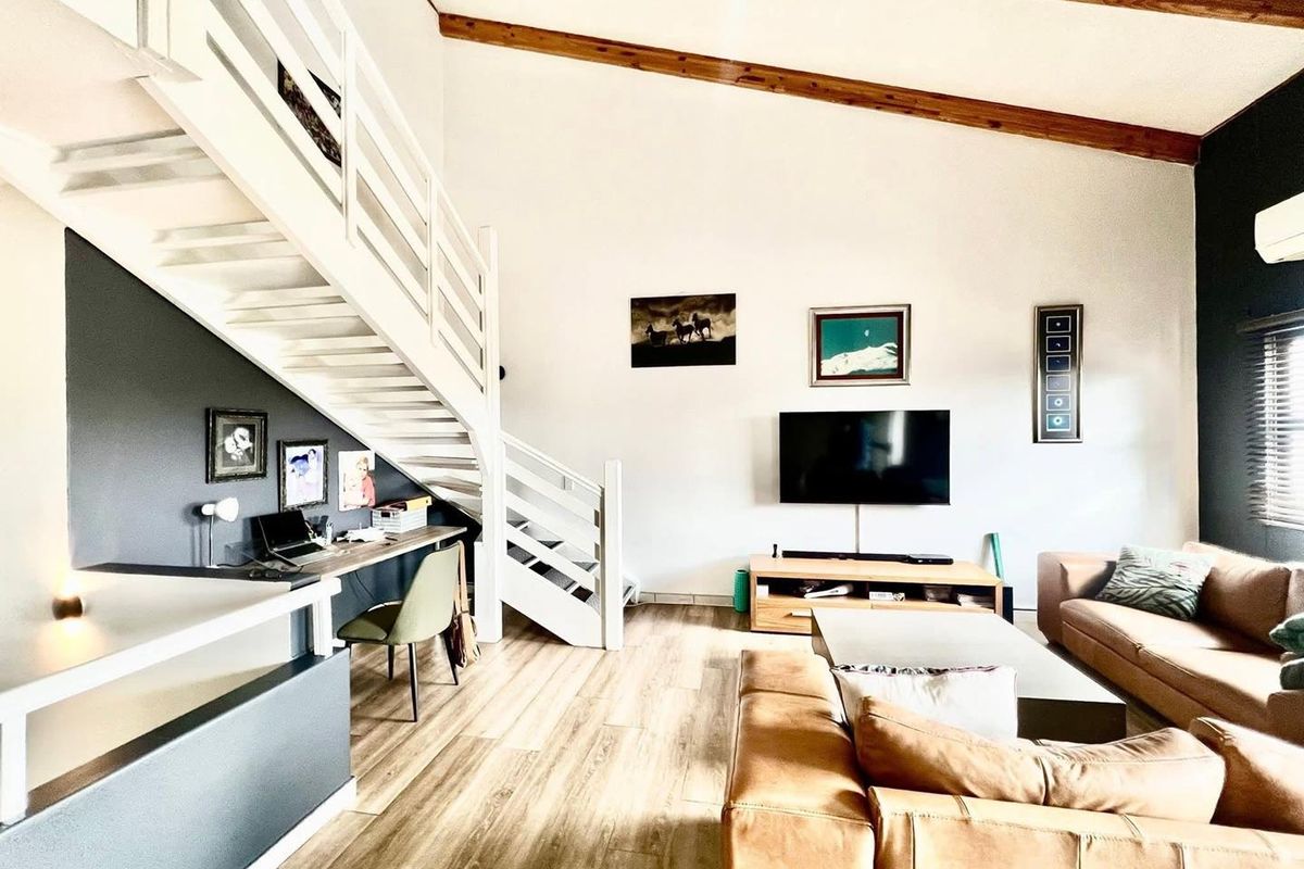 Spacious living room featuring high ceilings with exposed timber beams, a built-in staircase, and a dedicated workspace area.