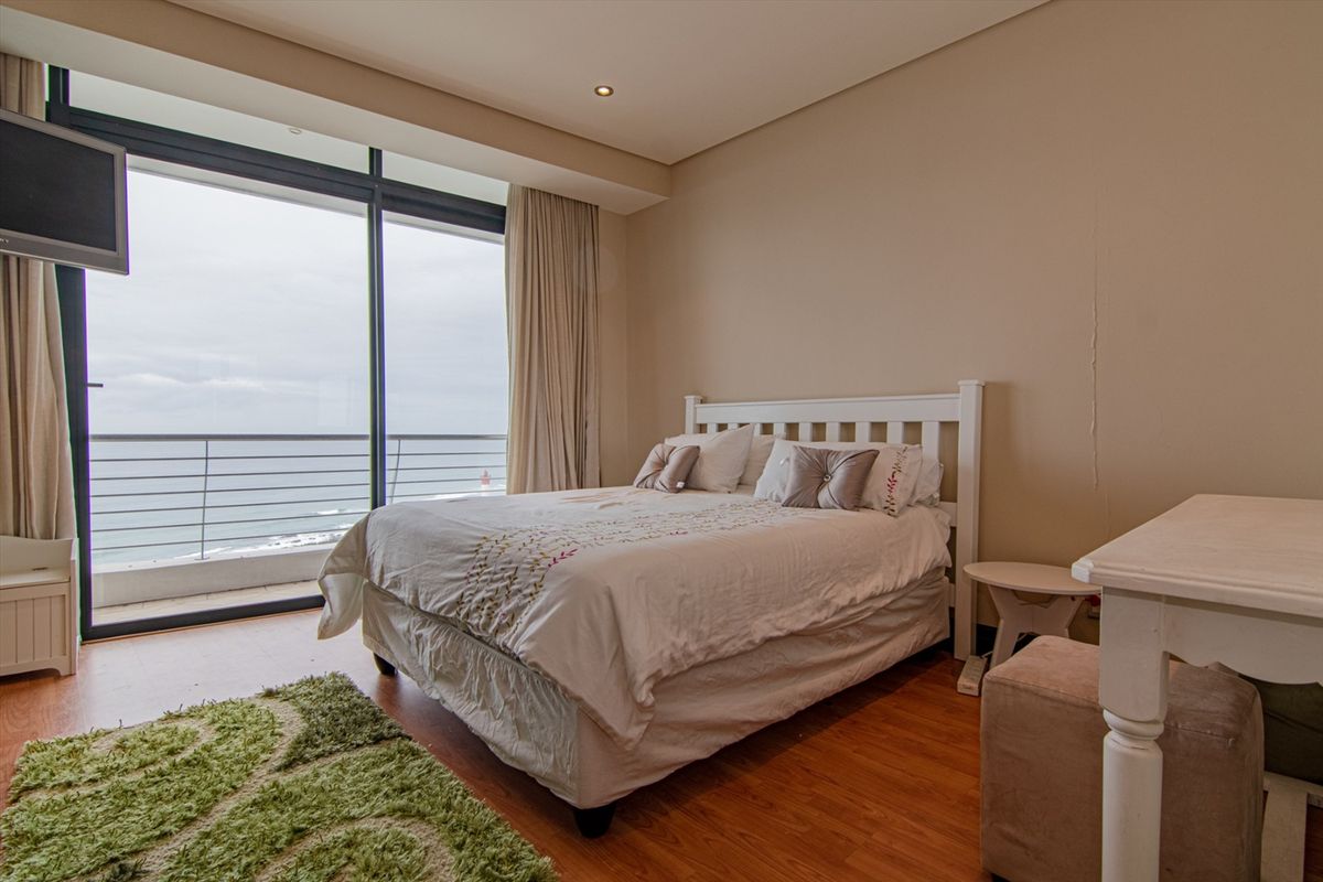 A bright bedroom featuring laminate flooring, recessed lighting, and large sliding glass doors opening onto a balcony with ocean views.