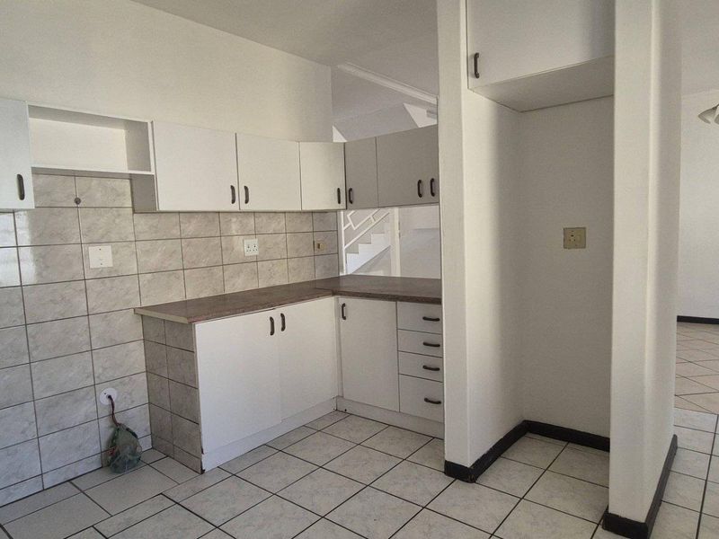 A functional, empty kitchen featuring white cabinetry, laminate countertops, and neutral ceramic tiling, offering a blank canvas for modern updates.