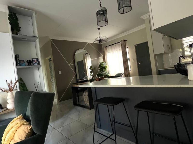 Modern open-plan living area featuring a kitchen island with stone countertops, tiled flooring, and contemporary pendant lighting, creating a cohesive and functional space.