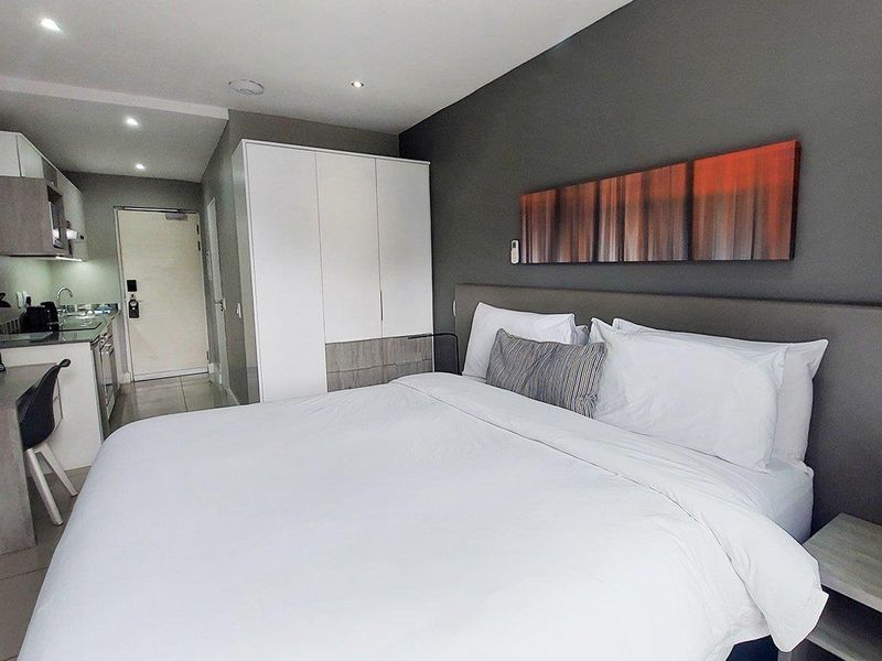 Modern open-plan studio apartment featuring a compact kitchenette, built-in wardrobe, and neutral finishes with contemporary recessed lighting.