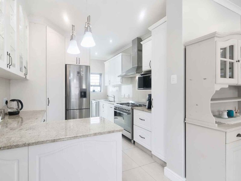 A bright, modern kitchen featuring white cabinetry, granite countertops, a gas stove with extractor fan, and high-quality finishes throughout.