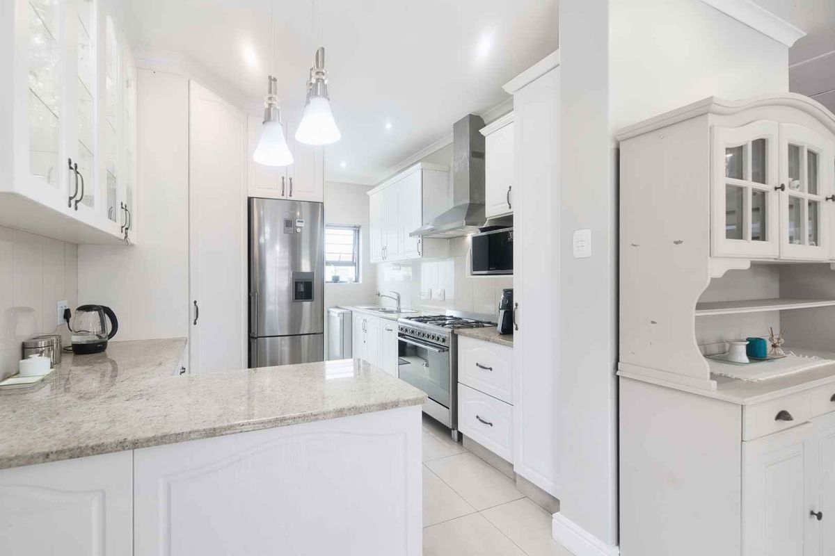 A bright, modern kitchen featuring white cabinetry, granite countertops, a gas stove with extractor fan, and high-quality finishes throughout.