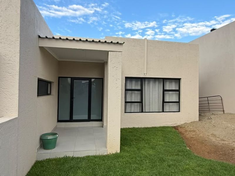 Rear view of the property featuring a covered patio, tiled flooring, and a well-maintained lawn with adjacent unfinished landscaping.