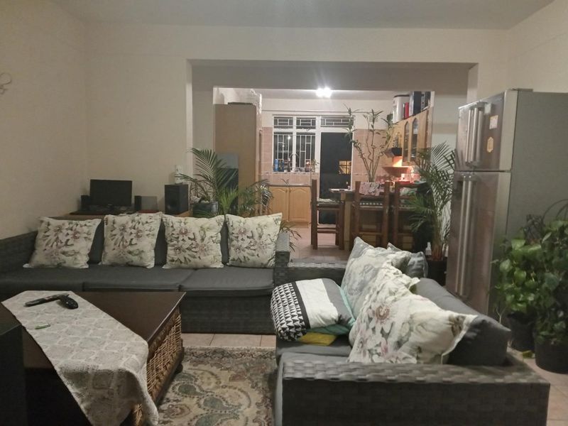 Open plan living area flowing into a kitchen with built-in cabinetry and security window bars.