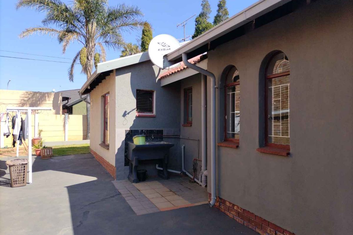 Rear exterior view of the property featuring a paved patio area, a fixed concrete wash basin, and arched window frames.