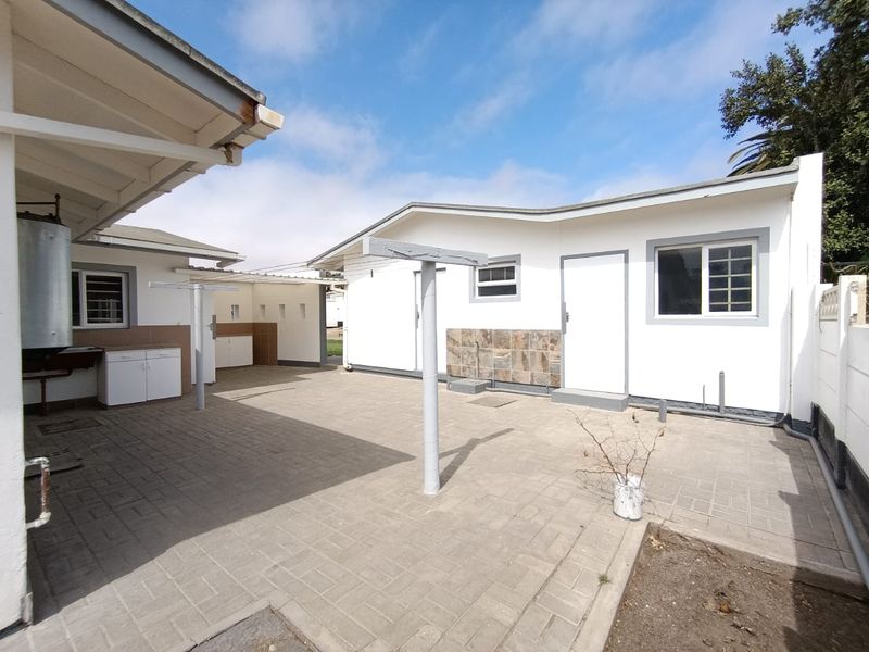 A paved rear courtyard area featuring an external washing line, utility sink, and access to the main dwelling and outbuilding structures.