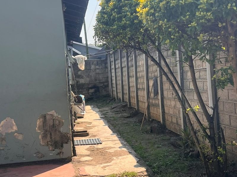 A narrow rear exterior side passage featuring a precast concrete boundary wall and a concrete pathway requiring maintenance and repair.