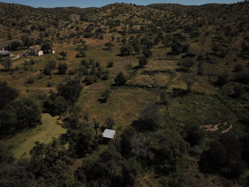 Aerial view of a rural property featuring open land, natural vegetation, a small outbuilding, and existing fencing infrastructure.