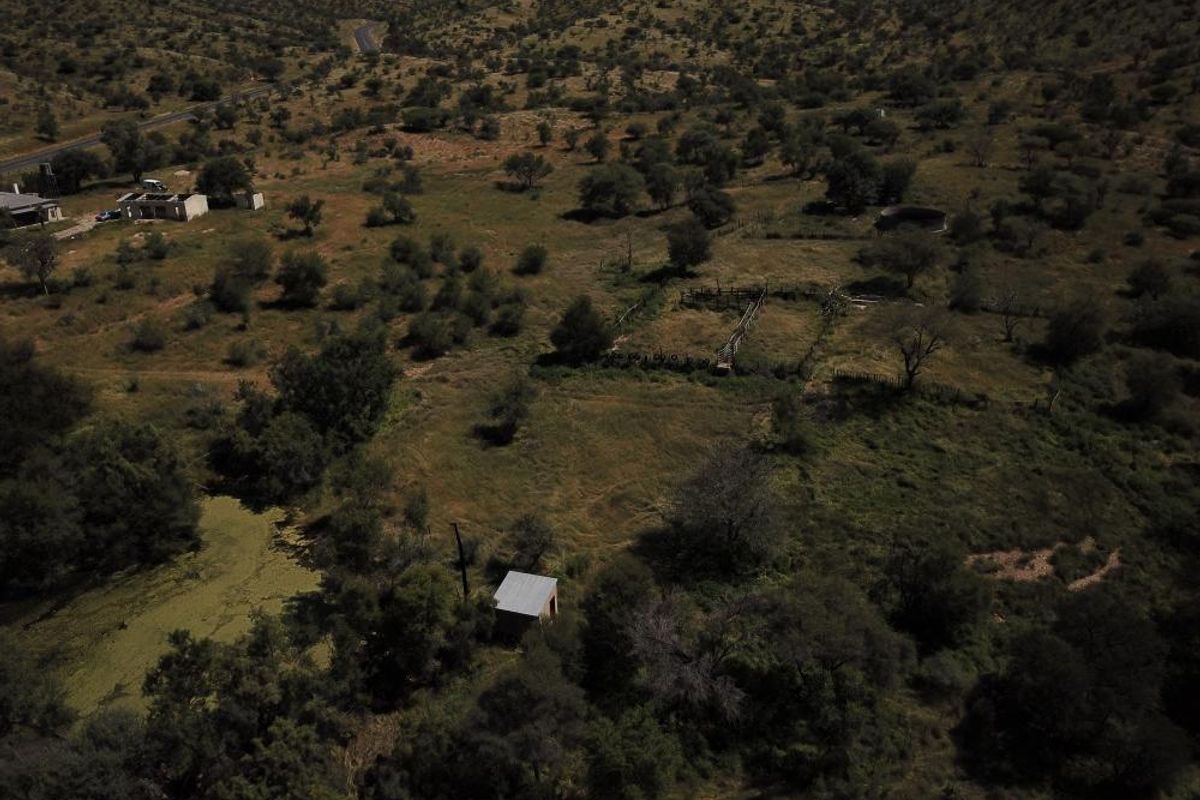Aerial view of a rural property featuring open land, natural vegetation, a small outbuilding, and existing fencing infrastructure.