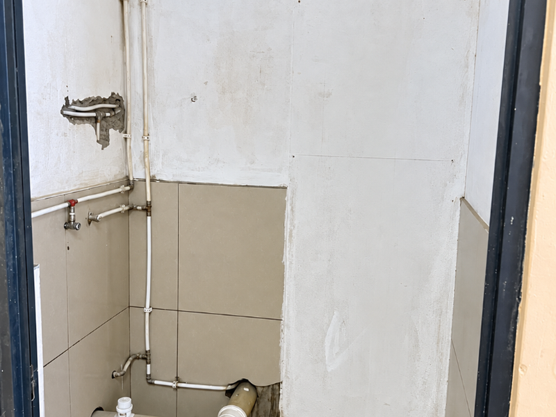 A small utility or laundry area featuring exposed plumbing and drainage connections, currently in an unfinished state requiring wall and finish repairs.