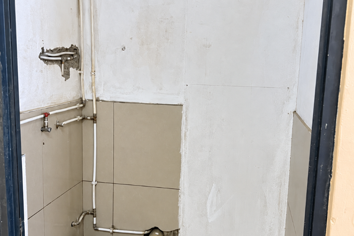 A small utility or laundry area featuring exposed plumbing and drainage connections, currently in an unfinished state requiring wall and finish repairs.