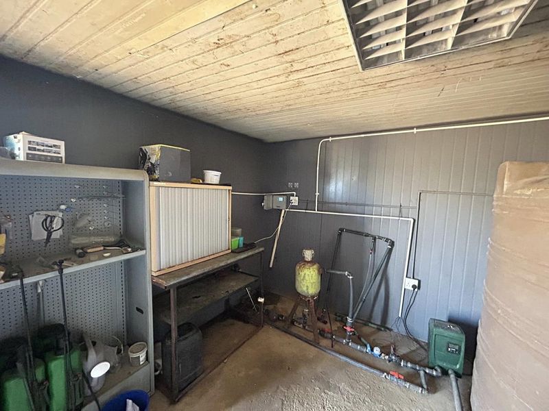 A functional utility space featuring exposed plumbing, a pressure pump system, and a timber ceiling, suitable for storage or workshop use.