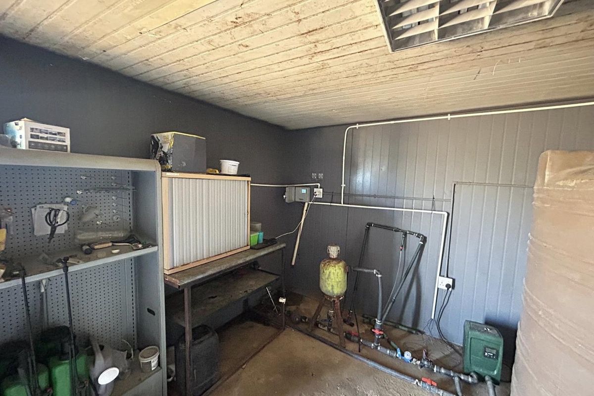 A functional utility space featuring exposed plumbing, a pressure pump system, and a timber ceiling, suitable for storage or workshop use.