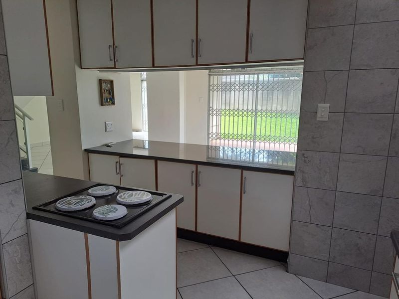 A functional kitchen featuring built-in cabinetry, dark laminate countertops, an electric hob, and tiled flooring with a view towards the garden.