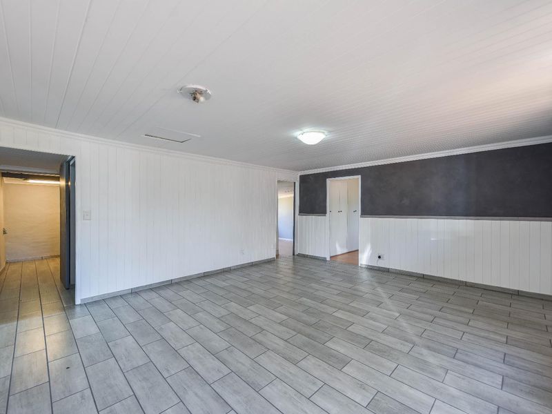 Spacious, empty living area featuring neutral wall paneling, modern grey floor tiles, and a split system air conditioner.