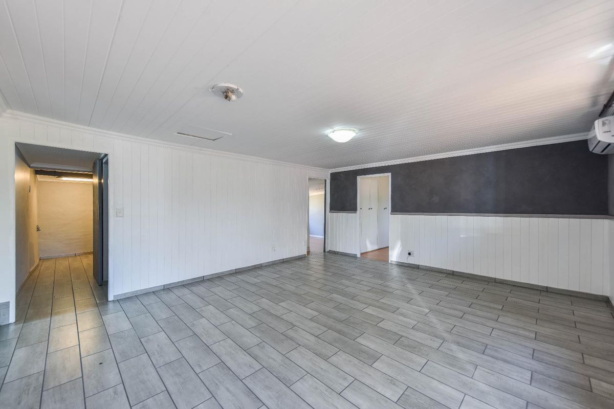 Spacious, empty living area featuring neutral wall paneling, modern grey floor tiles, and a split system air conditioner.