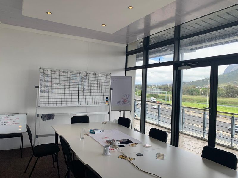A bright office meeting room featuring floor-to-ceiling windows with views, recessed lighting, and a modern suspended ceiling bulkhead.