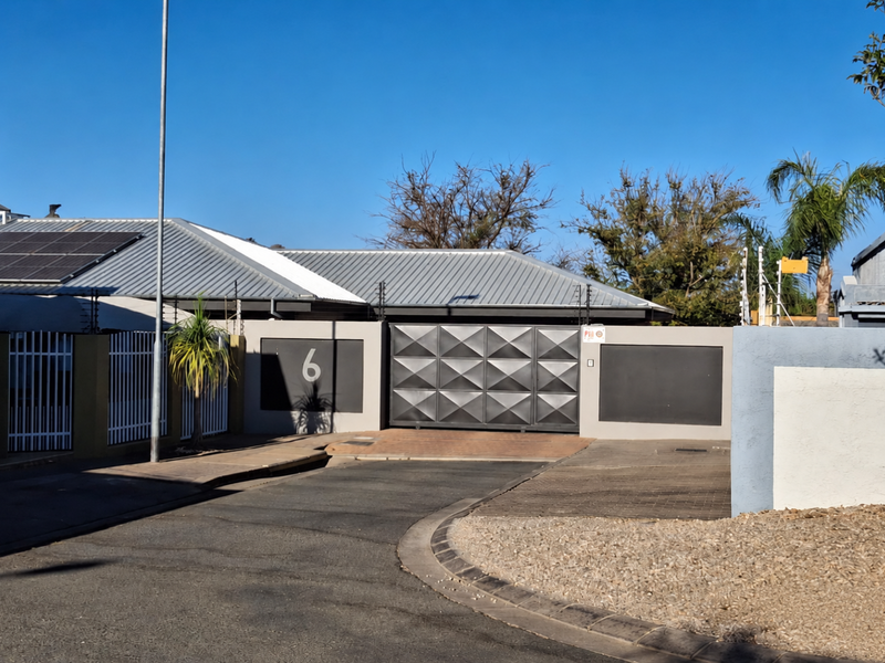 Front elevation of the property featuring a modern sliding gate, paved driveway, and solar panels installed on the metal roof.