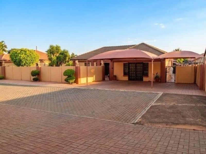 Front exterior view of the property featuring a paved driveway, double carport, and secure boundary walling.