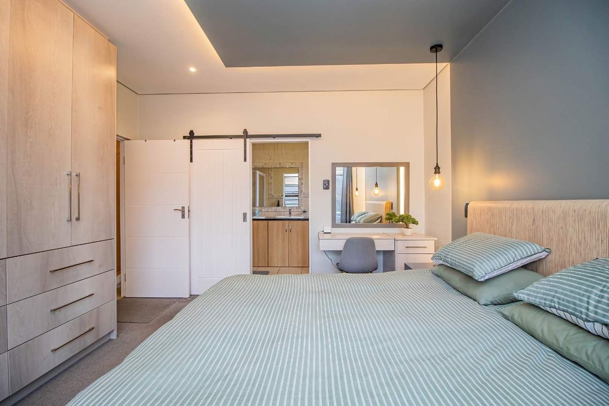 Modern bedroom featuring a built-in wardrobe, recessed ceiling with ambient lighting, and a sliding barn door leading to an en-suite bathroom.