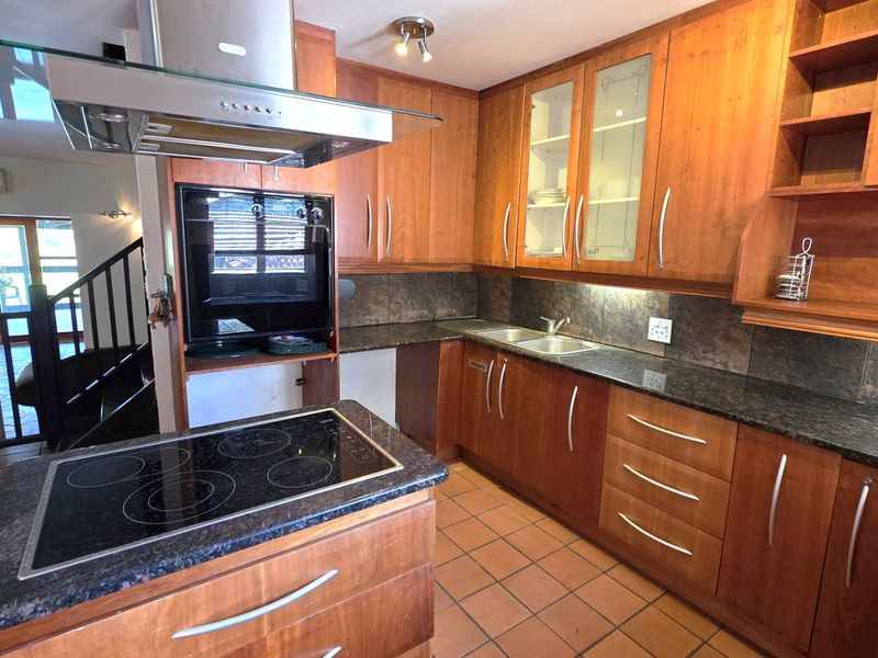 A functional kitchen featuring warm-toned wooden cabinetry, granite countertops, a central island with an electric hob, and integrated appliances.