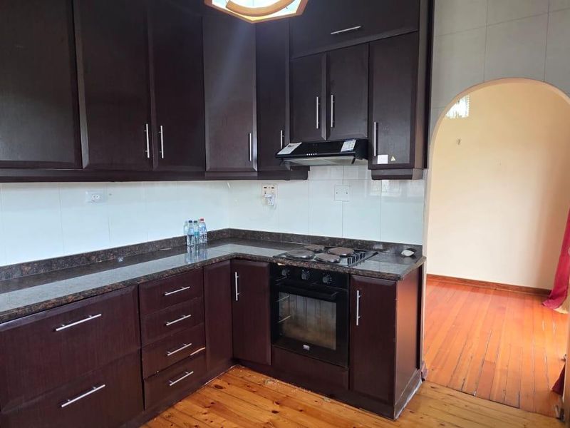 A functional kitchen featuring dark wood cabinetry, granite countertops, built-in oven, gas hob, and extractor fan, with hardwood flooring and an arched entryway.