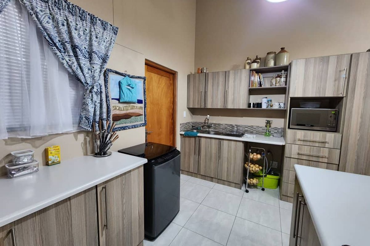 A functional kitchen featuring wood-grain cabinetry, tiled flooring, a double sink, and built-in microwave housing, offering practical storage and workspace.