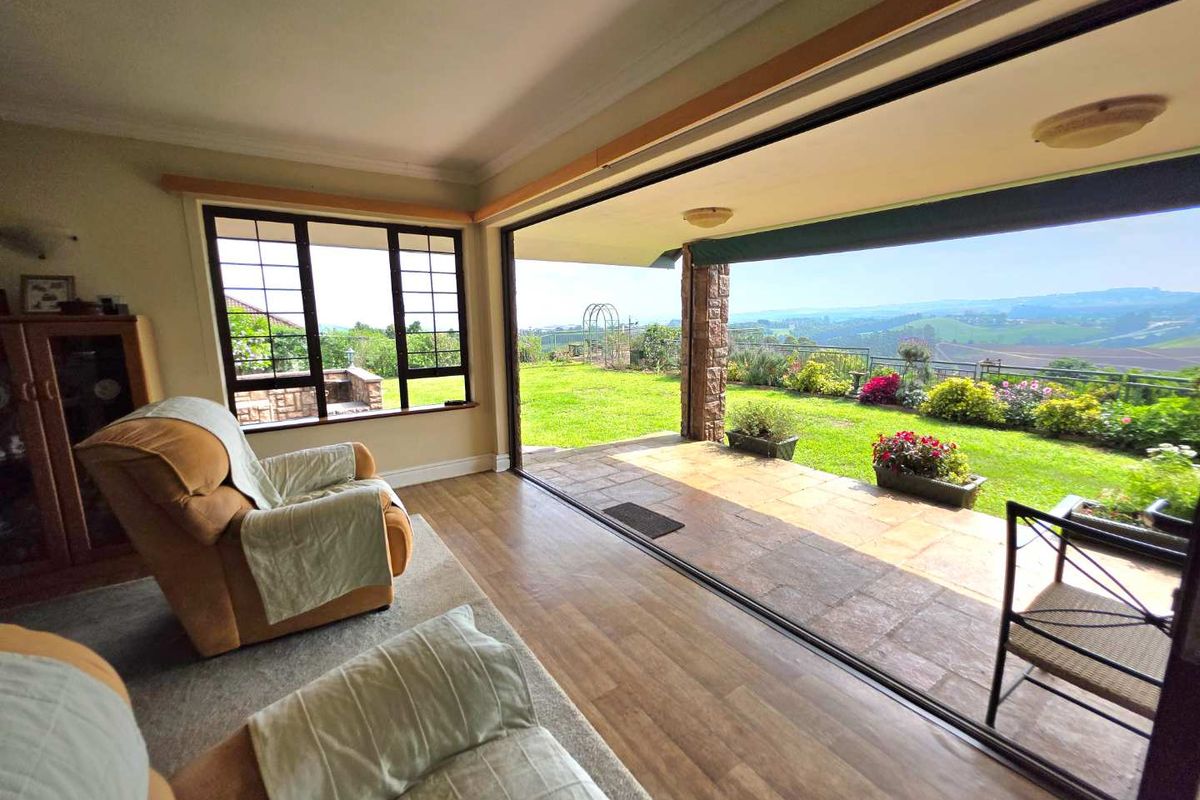 A bright living area featuring large sliding glass doors that open onto a covered patio with scenic garden and landscape views.