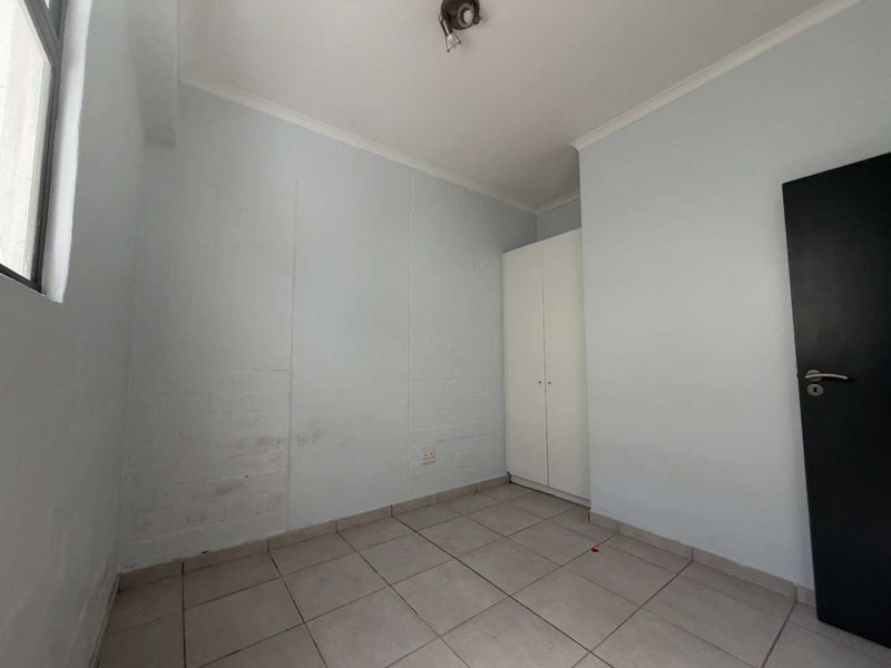 An empty bedroom featuring tiled flooring, a built-in wardrobe, and painted brick walls, offering a blank canvas for personalization.