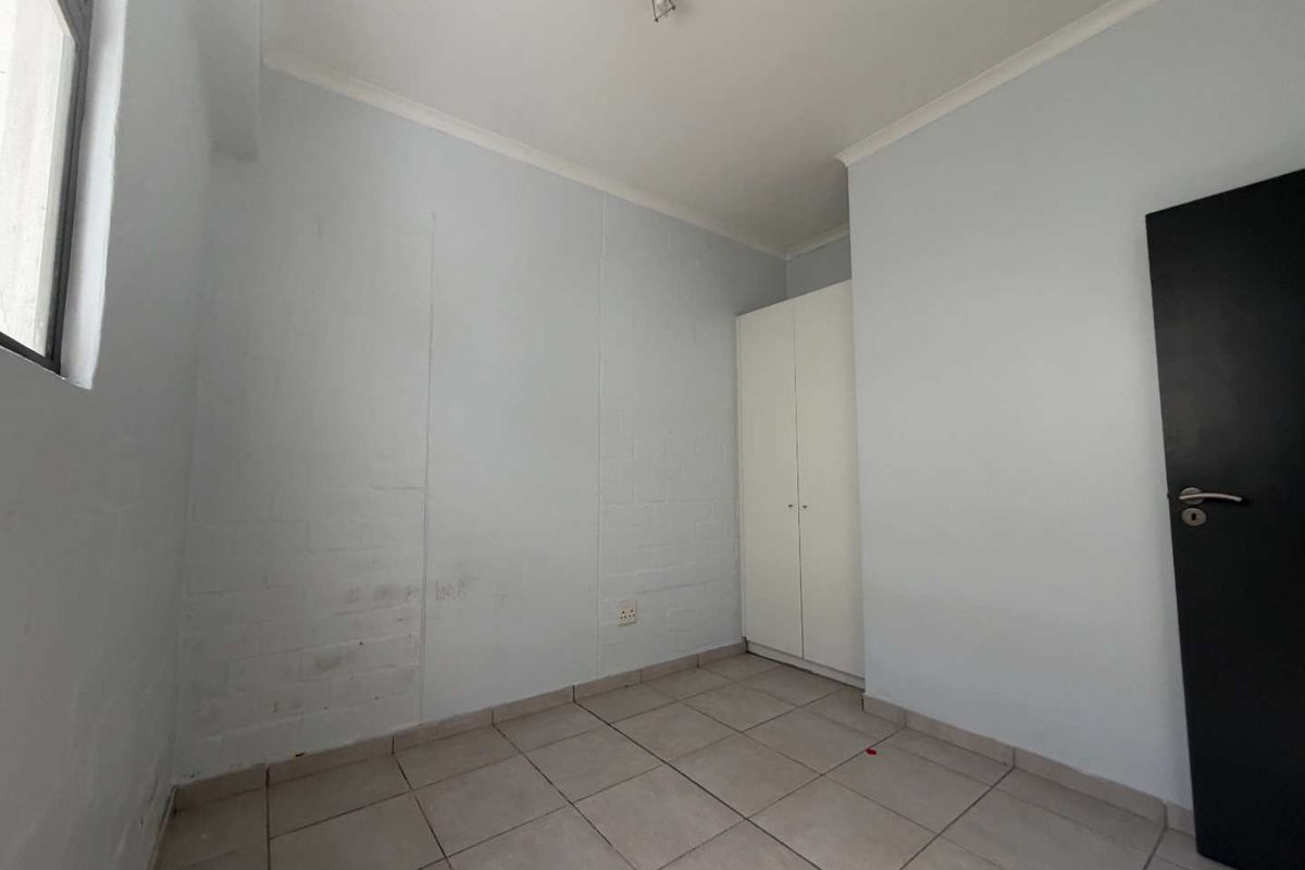 An empty bedroom featuring tiled flooring, a built-in wardrobe, and painted brick walls, offering a blank canvas for personalization.