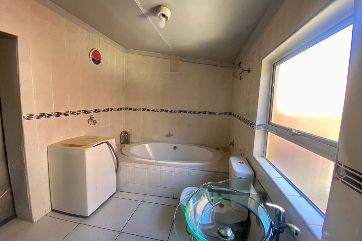 A dated bathroom featuring a built-in bathtub, tiled walls, and a glass vessel sink, requiring cosmetic updates to modernize the space.